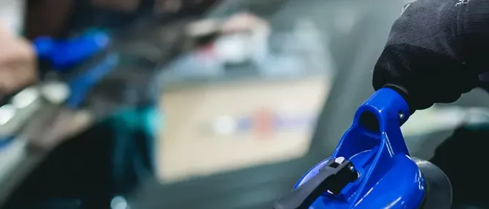 Technicien SOS Pare-Brise+ remplaçant un pare-brise à domicile devant le garage d'un particulier